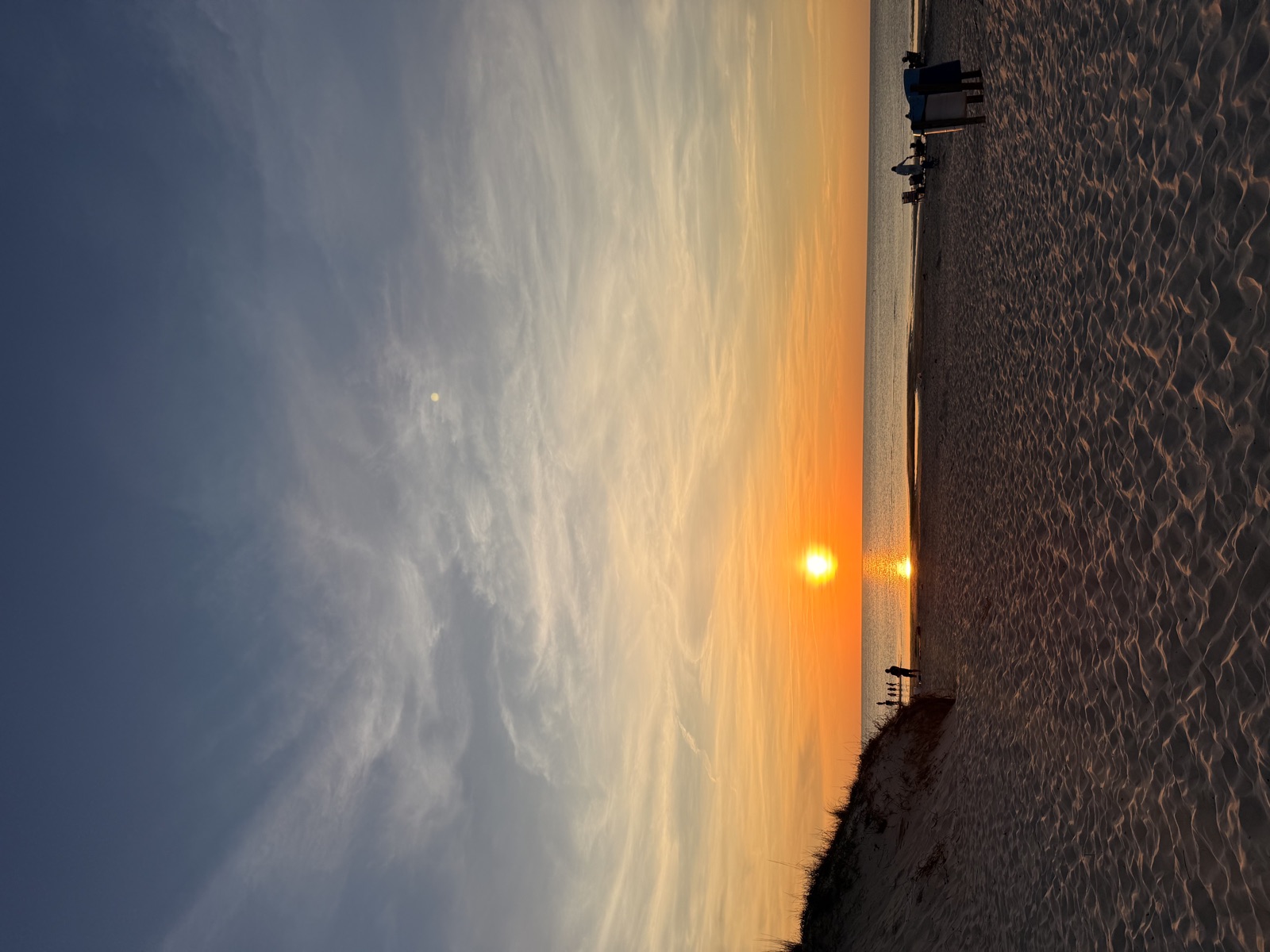 The sun setting over the water from behind a dune